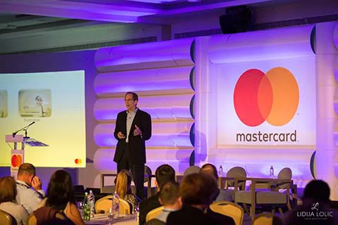 Business speaker presenting at Mastercard conference with audience.