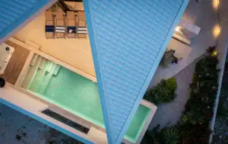 Aerial view of contemporary hotel pool area with sun loungers, outdoor spaces, and surrounding greenery.