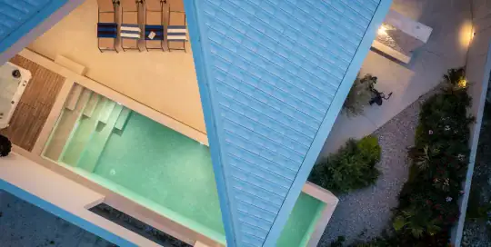 Aerial view of contemporary hotel pool area with sun loungers, outdoor spaces, and surrounding greenery.
