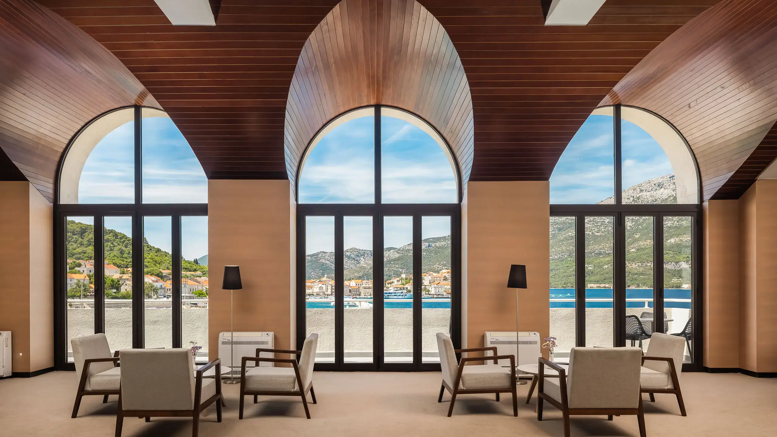 Modern hotel lobby with large arched windows and scenic waterfront view.