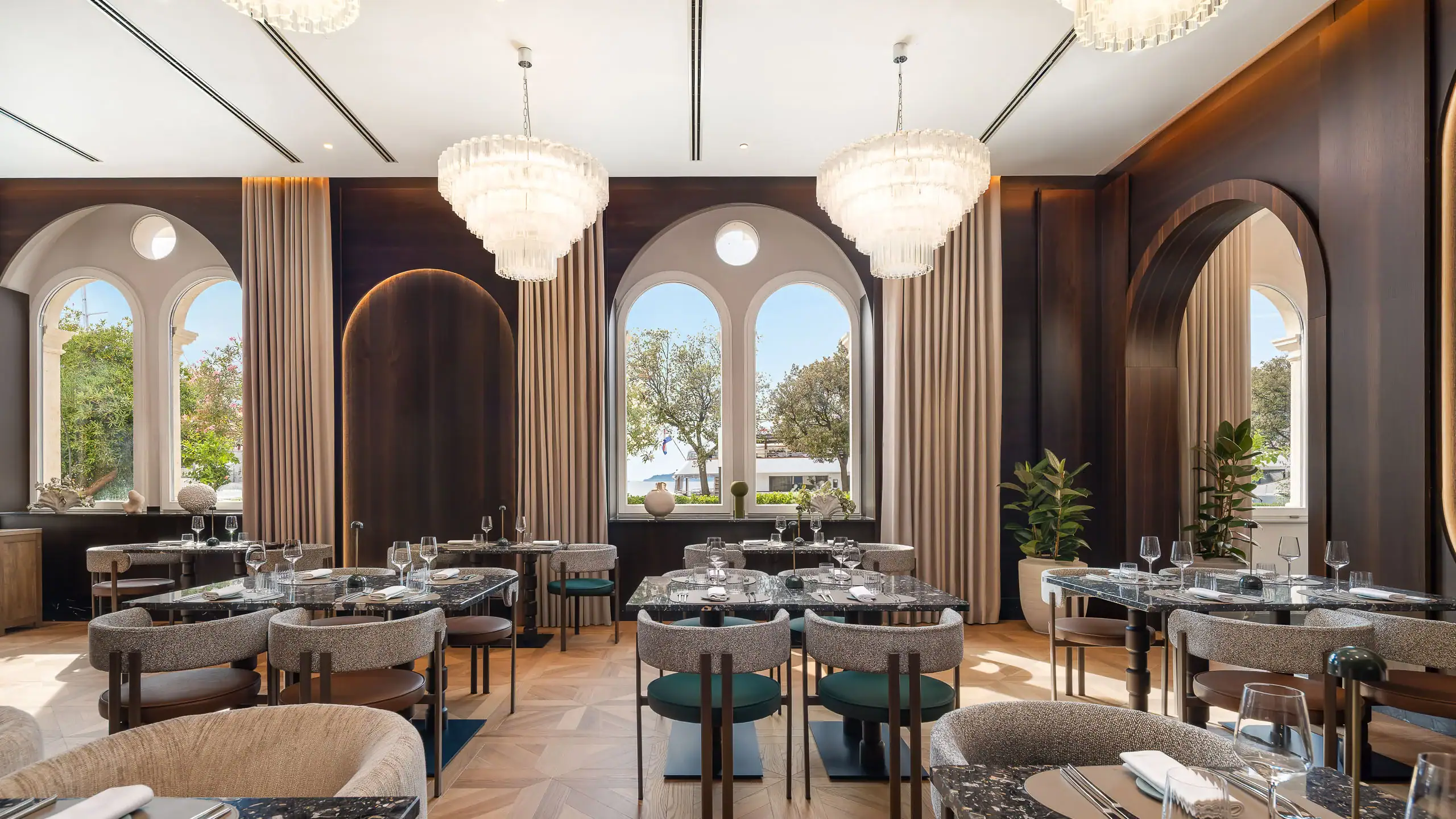 Luxurious hotel restaurant interior with chandeliers and large windows.