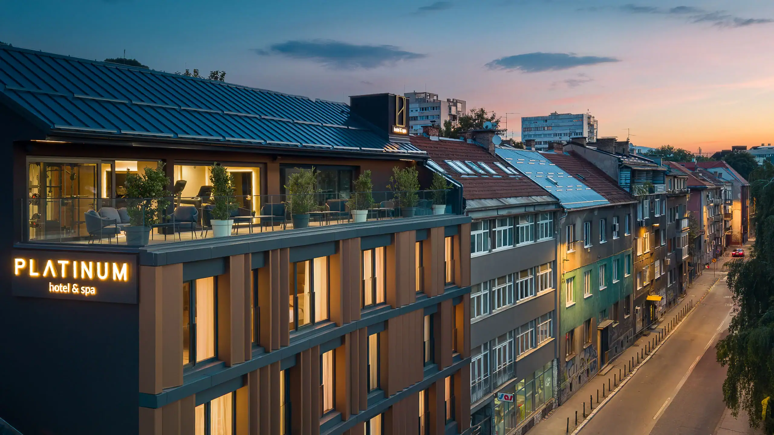 Contemporary hotel building with illuminated balconies and city view at sunset.